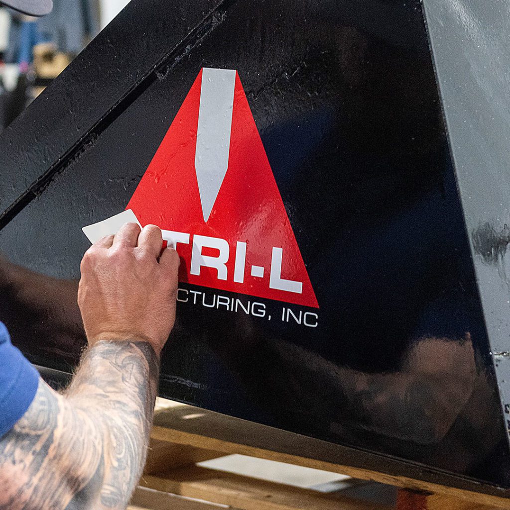 man cleans black bucket with Tri-L logo on side